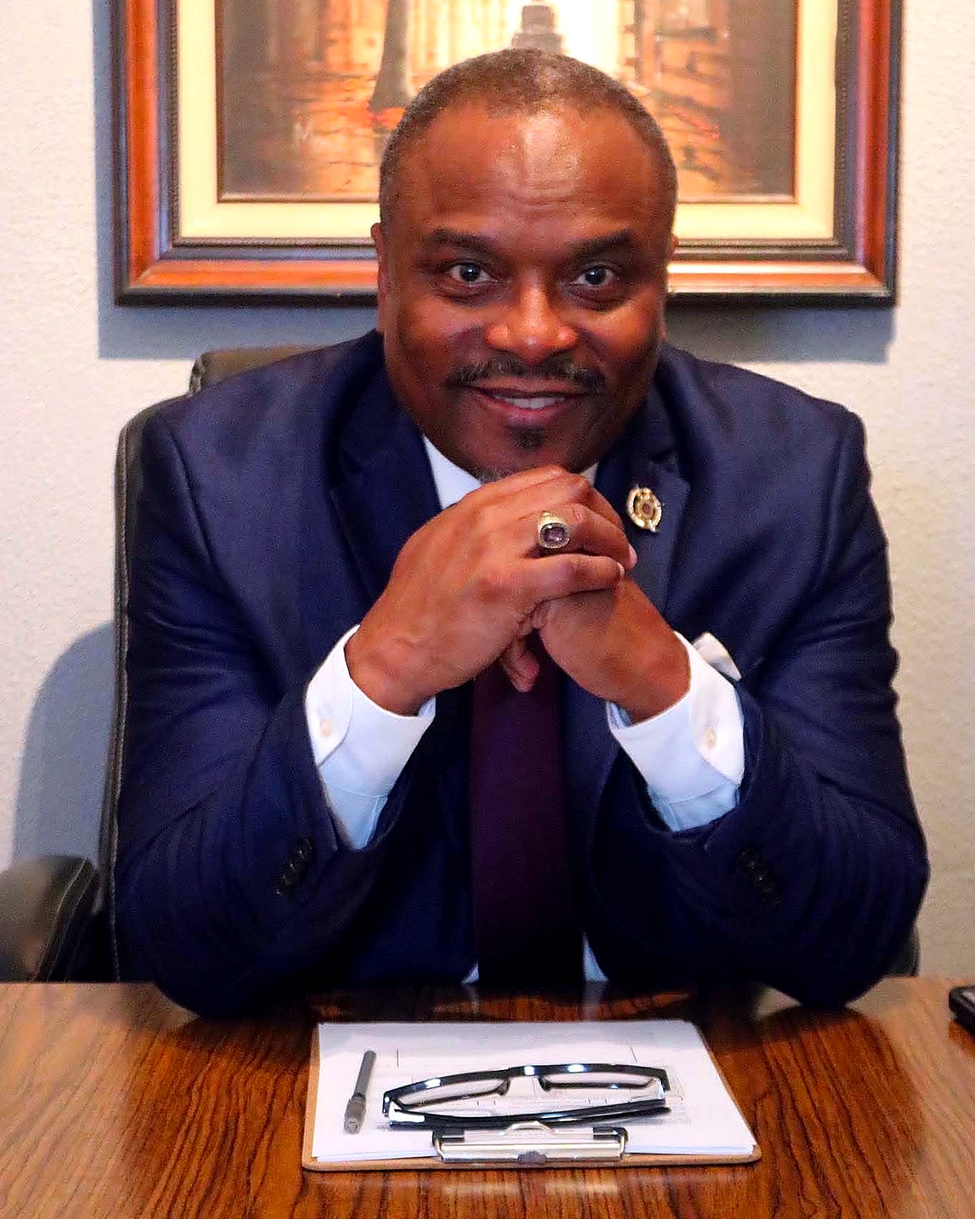 Richard Wooten smiling at his desk in a suit and burgundy tie.