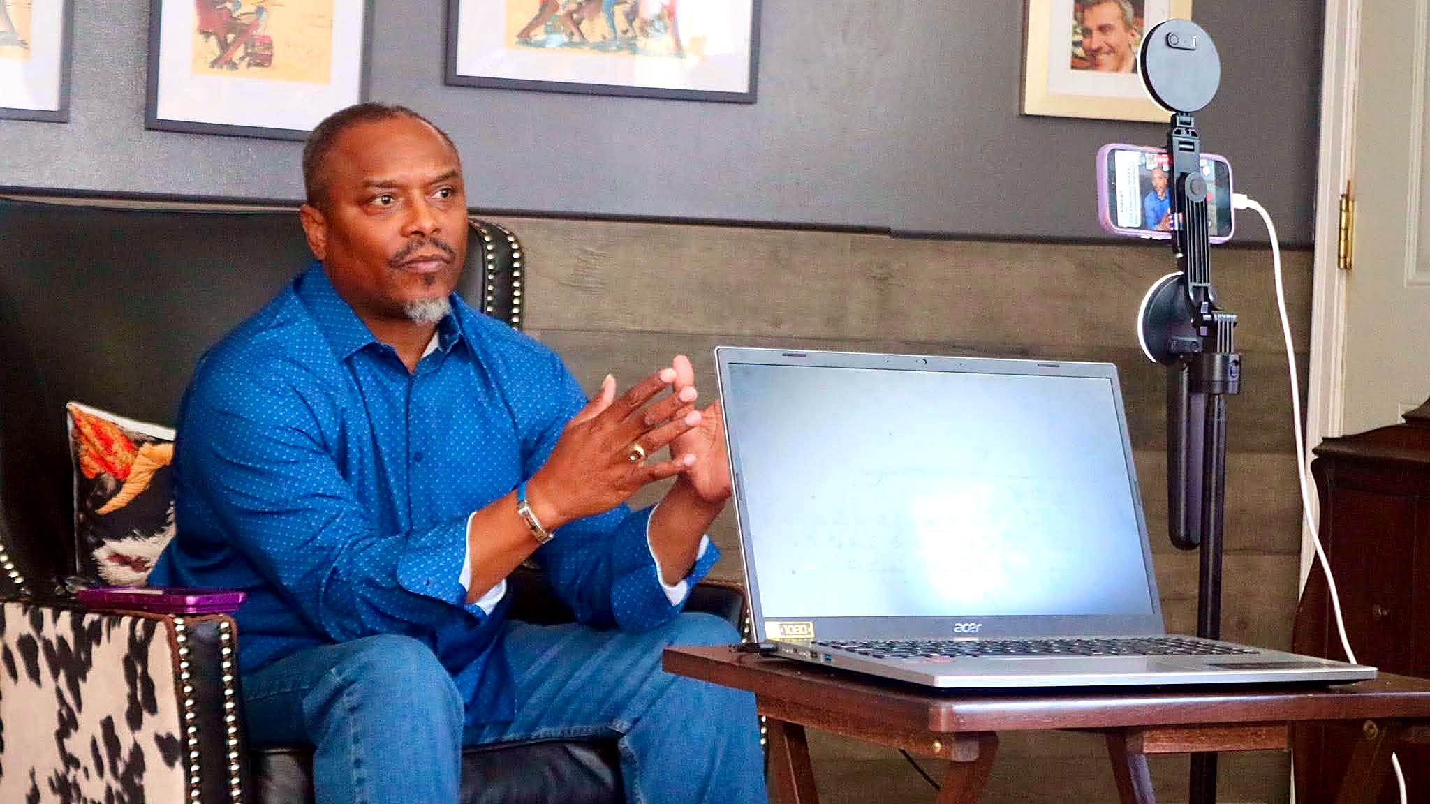 Richard Wooten gesturing beside a laptop and a phone on a recording stand.